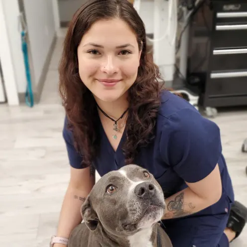 A veterinary employee posing with a smiling pitbull